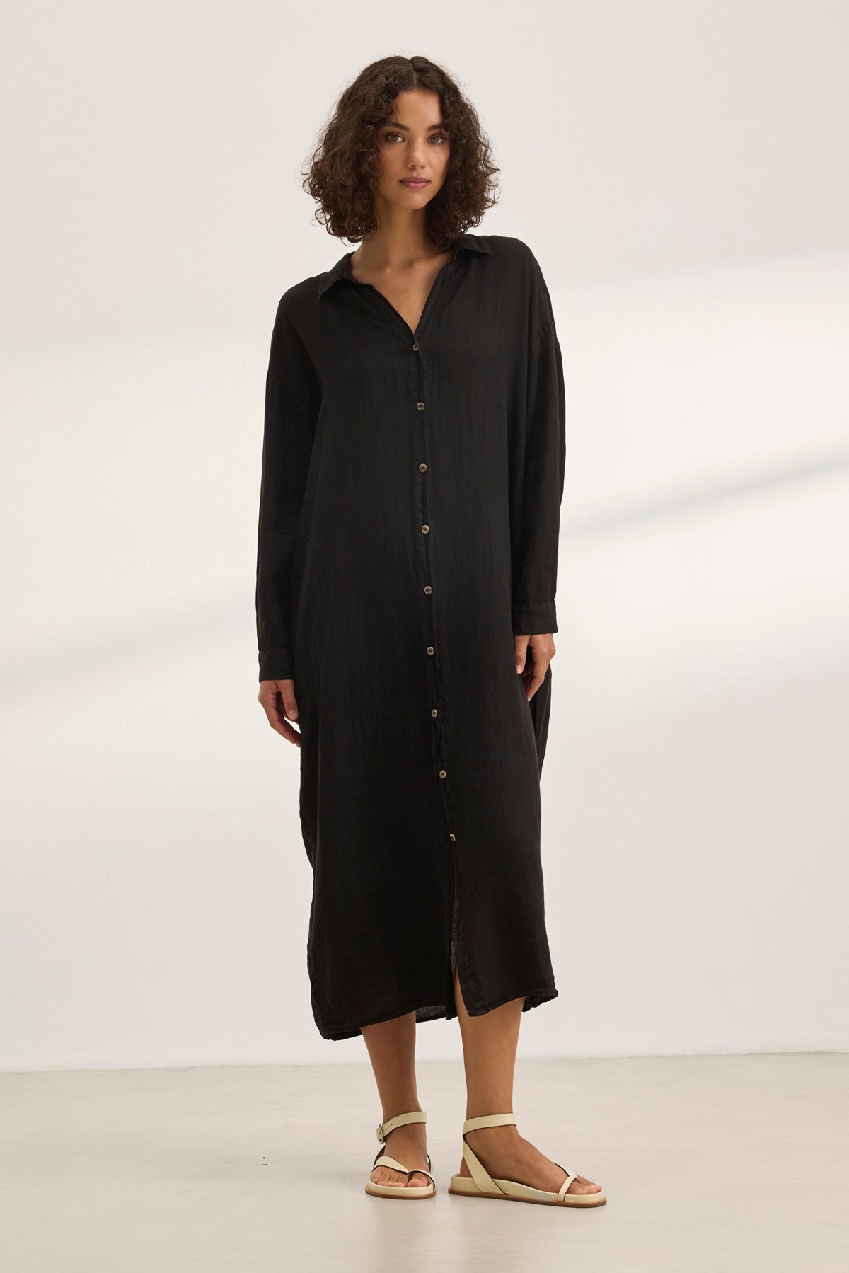   A person wearing the NICOLE LINEN DRESS by Velvet by Graham & Spencer and white sandals stands on a light floor against a plain backdrop, epitomizing breathable comfort. 