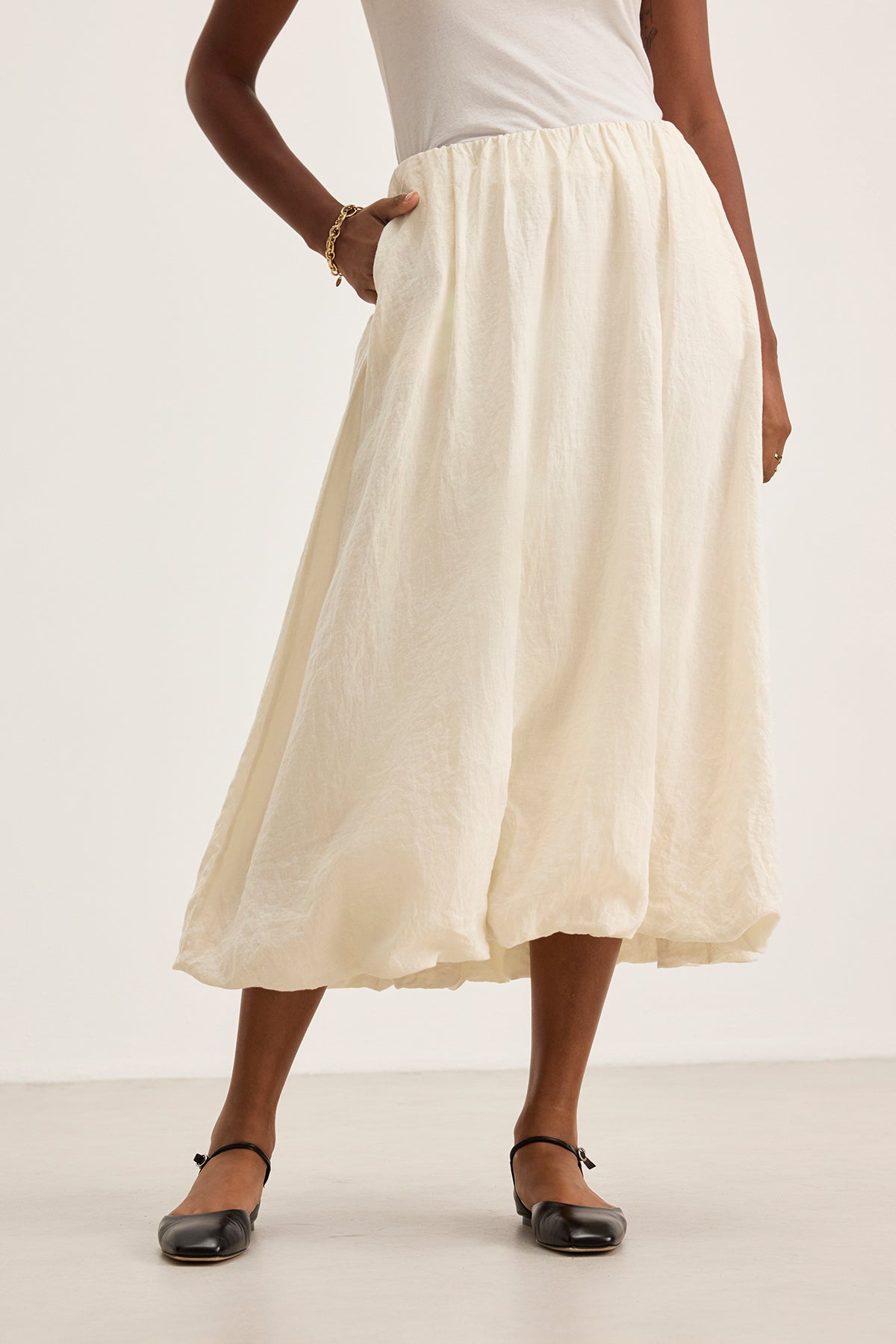 Someone in a white RACHELLE LINEN SKIRT by Velvet by Graham & Spencer, featuring a bubble hem, pairs it with a white top and black shoes, casually resting one hand in the skirt pocket.-38663160529089