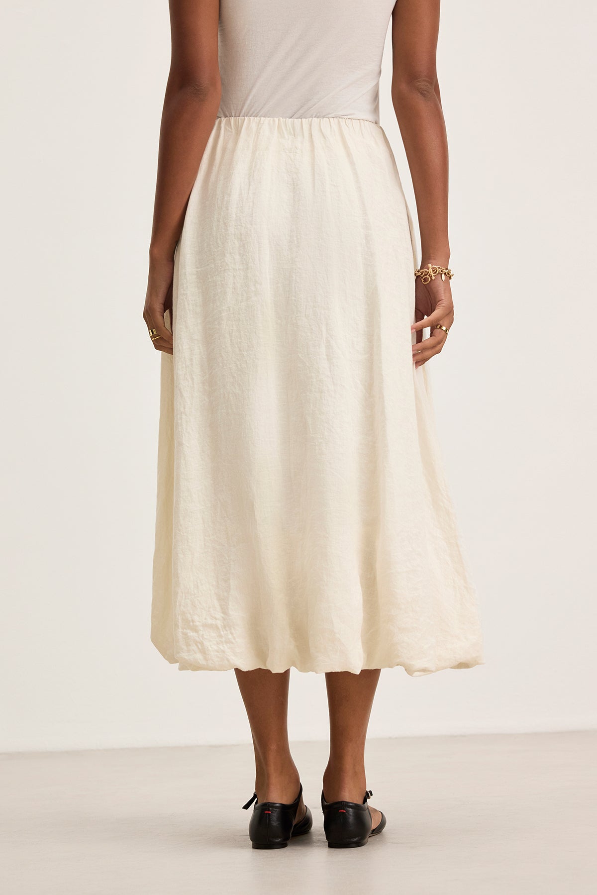   A person stands with hands by their sides, wearing a white sleeveless top and the Velvet by Graham & Spencer RACHELLE LINEN SKIRT, a woven linen midi skirt featuring an elastic waist. 