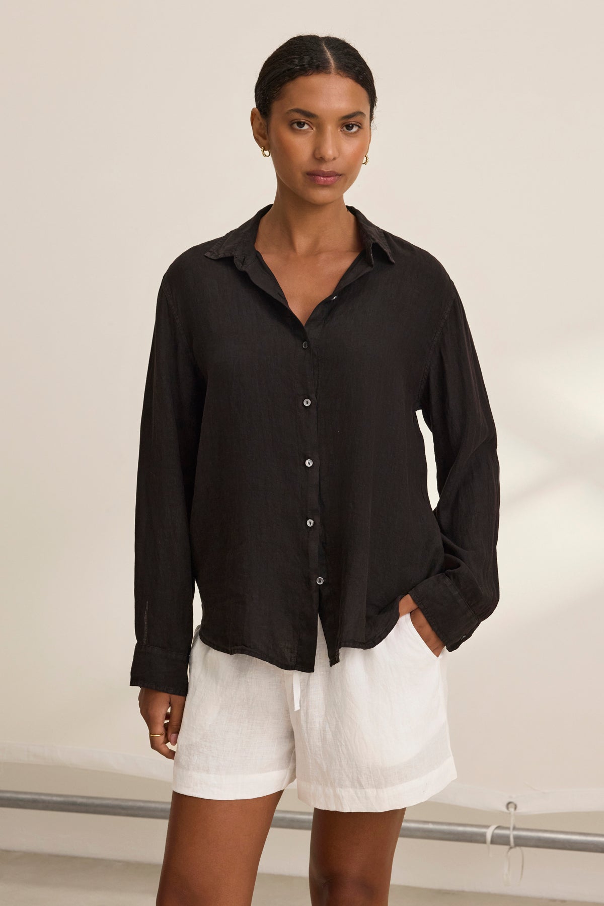 A person wearing the Velvet by Graham & Spencer SISI LINEN SHIRT in black pairs it with white shorts, all set against a neutral background for an effortlessly chic look.-38819774202049