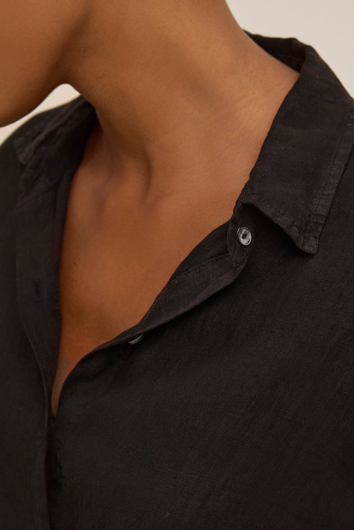   Close-up of a person in the breathable SISI LINEN SHIRT by Velvet by Graham & Spencer, featuring a lightweight woven design with one button undone and the collar slightly open, highlighting the neck and shoulder area. 