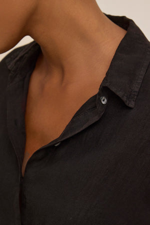 Close-up of a person in the breathable SISI LINEN SHIRT by Velvet by Graham & Spencer, featuring a lightweight woven design with one button undone and the collar slightly open, highlighting the neck and shoulder area.