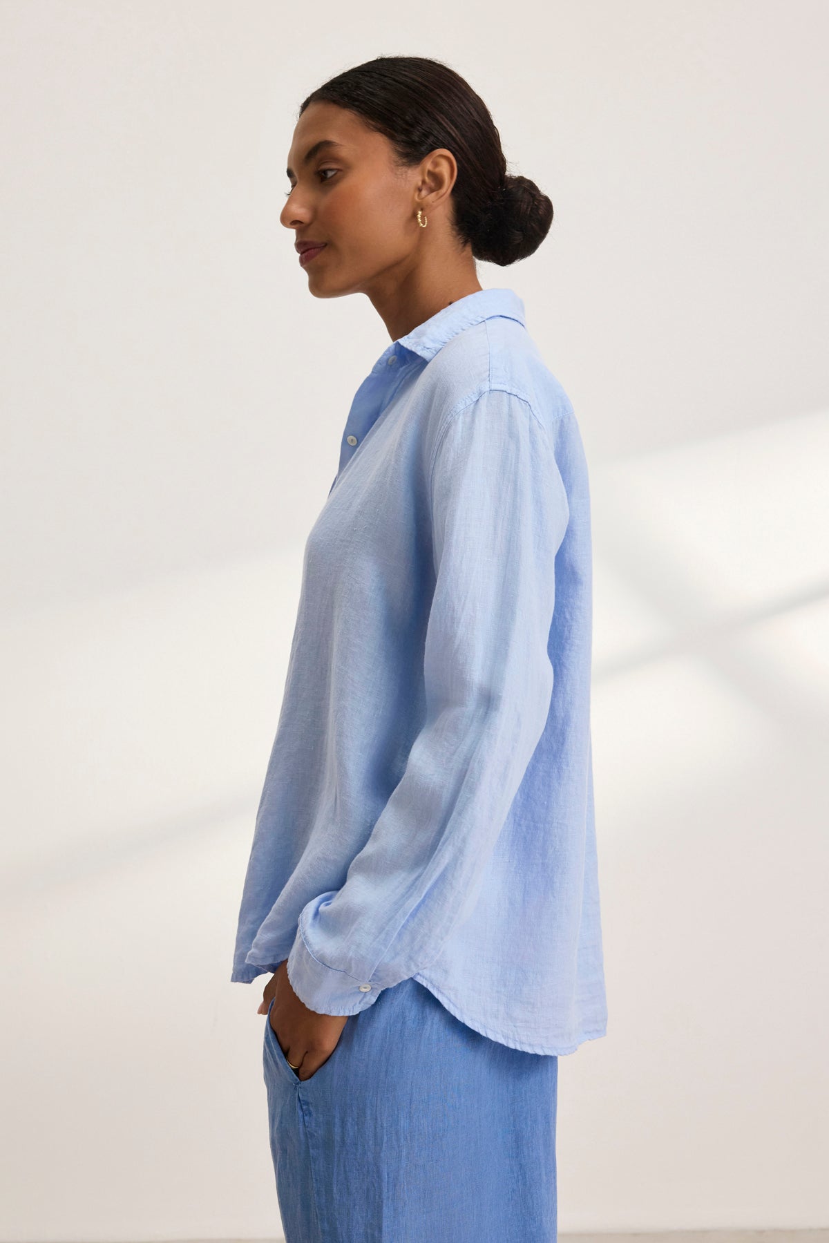   Profile view of a person wearing the light blue SISI LINEN SHIRT from Velvet by Graham & Spencer, offering a breathable fit against a neutral backdrop. 