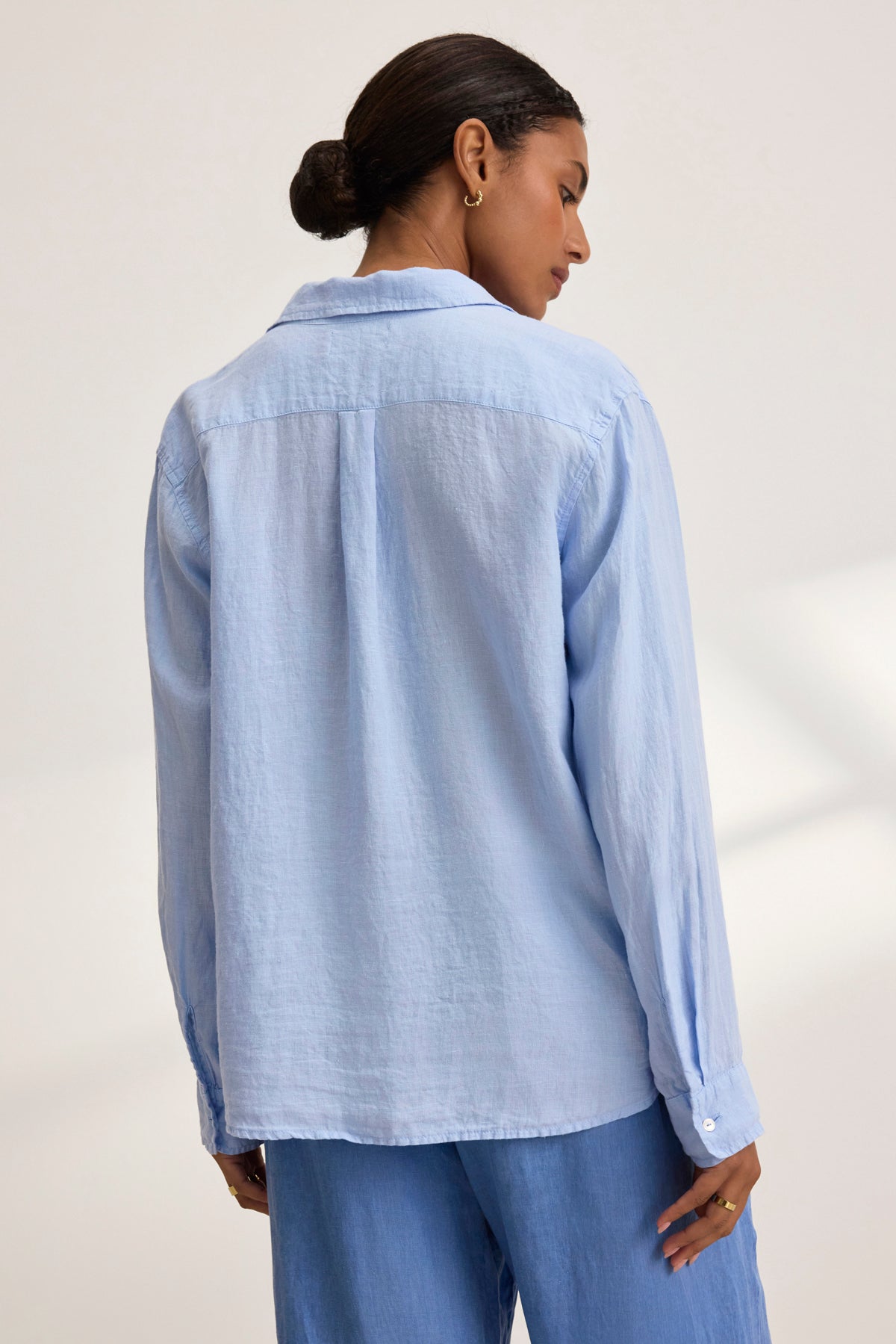   A person with tied-back hair wears a SISI LINEN SHIRT in light blue by Velvet by Graham & Spencer, seen from behind. 