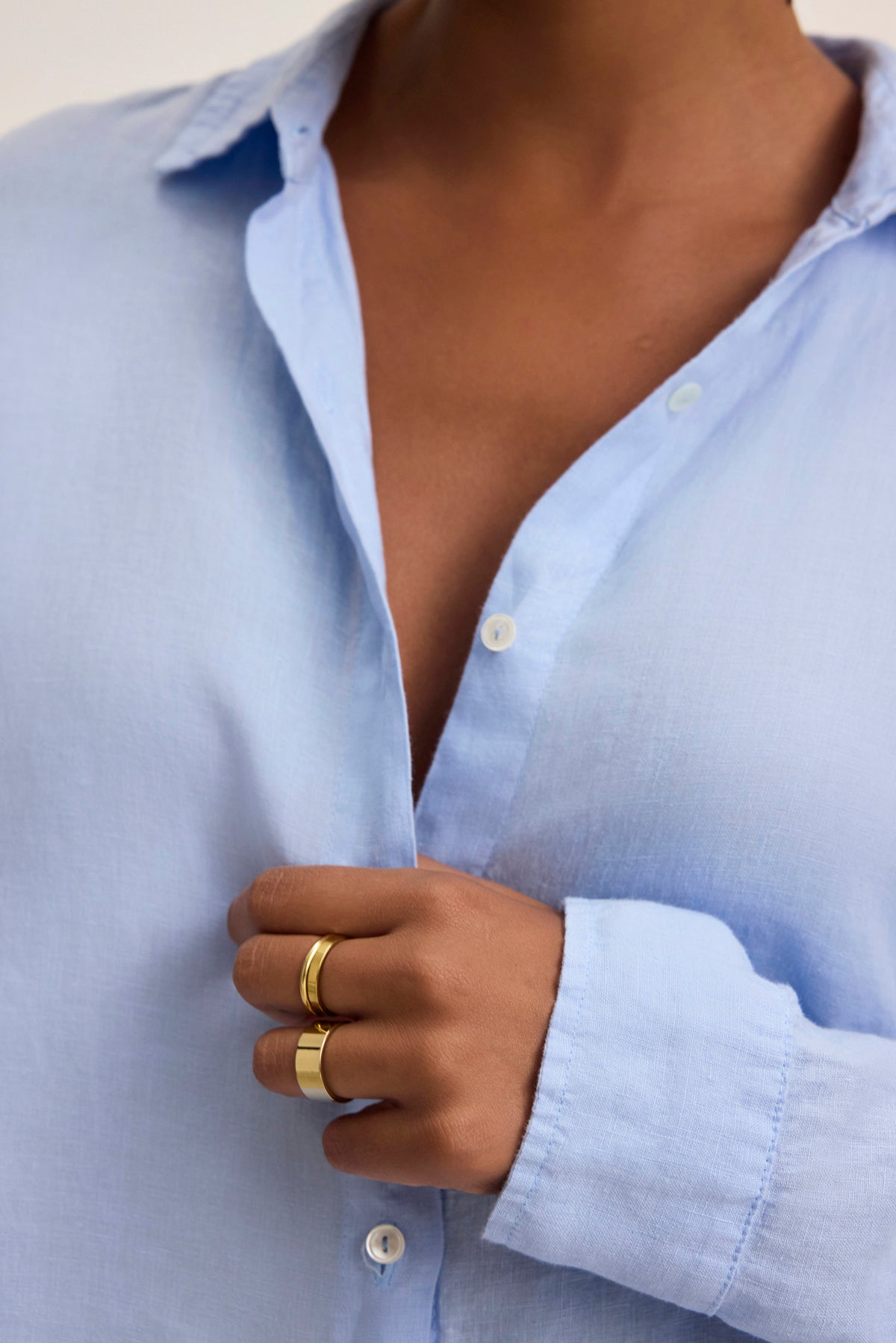   Wearing the SISI LINEN SHIRT by Velvet by Graham & Spencer in light blue, with the top buttons casually undone and gold rings on display, captures a breezy and breathable style. 