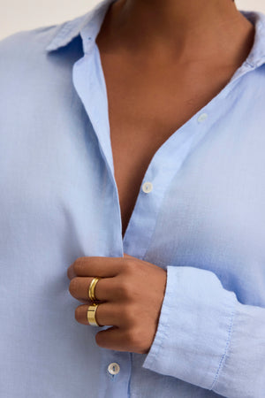 Wearing the SISI LINEN SHIRT by Velvet by Graham & Spencer in light blue, with the top buttons casually undone and gold rings on display, captures a breezy and breathable style.