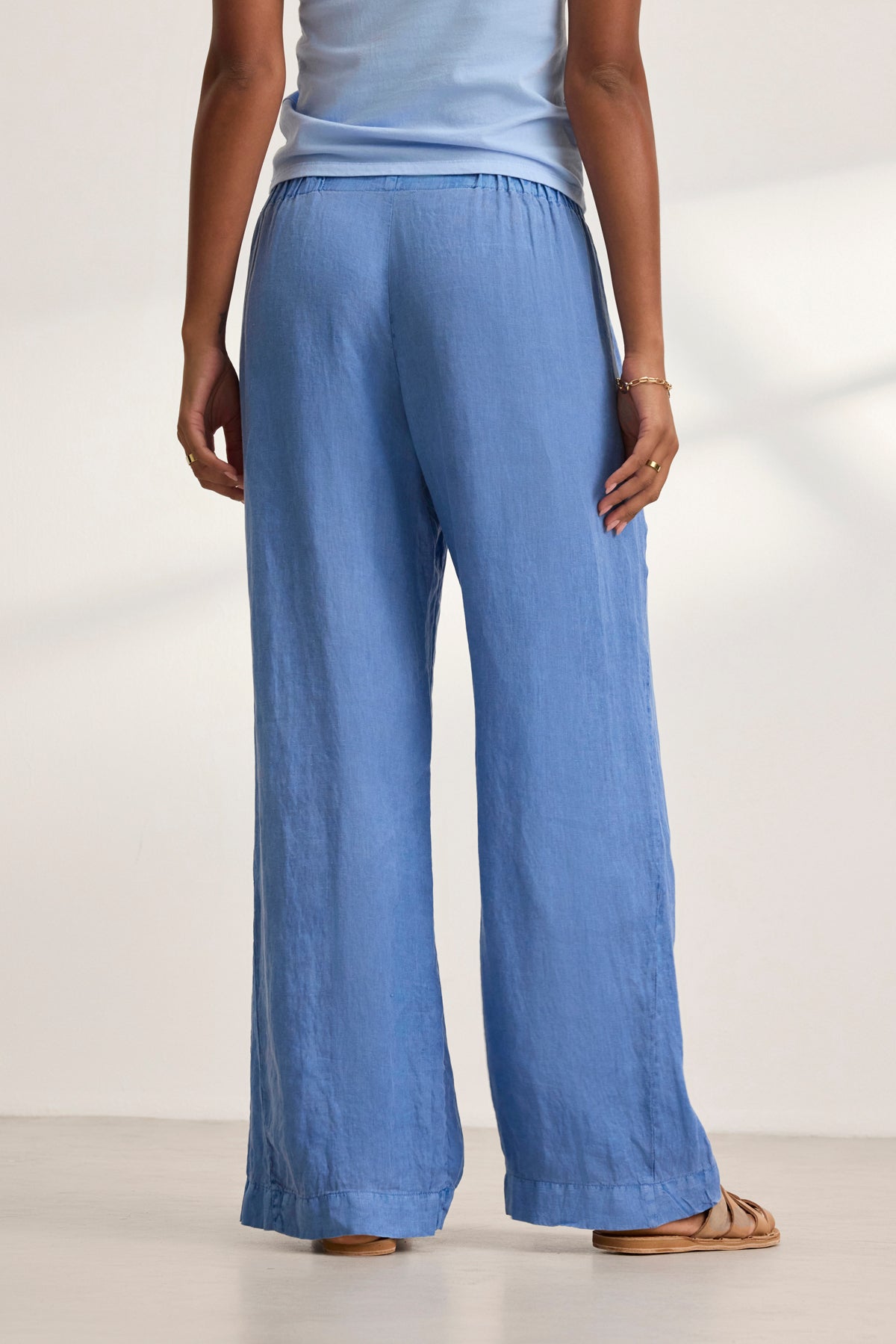 A person wearing the Velvet by Graham & Spencer STEPHANIE LINEN PANT in a relaxed fit paired with a matching top, standing barefoot on a light floor, facing away.-38819778756801