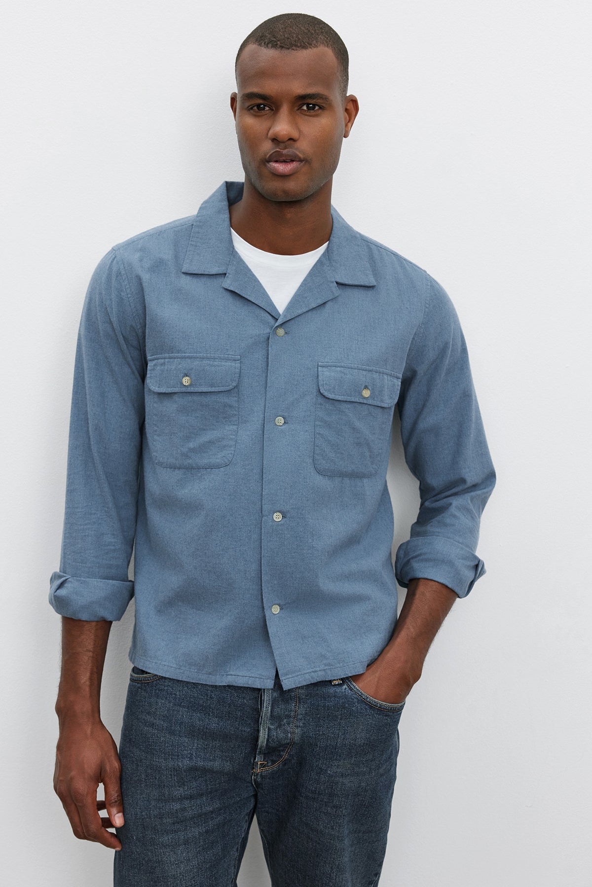   A man wearing the DONOVAN BUTTON-UP SHIRT in light blue cotton blend twill by Velvet by Graham & Spencer over a white T-shirt and jeans stands against a plain white background. 