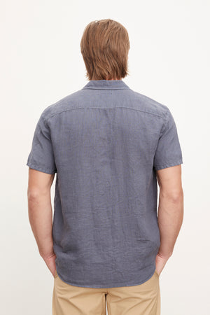 A person with shoulder-length blond hair is shown from the back, wearing a MACKIE LINEN BUTTON-UP SHIRT by Velvet by Graham & Spencer and beige pants, perfect for a summer wardrobe.