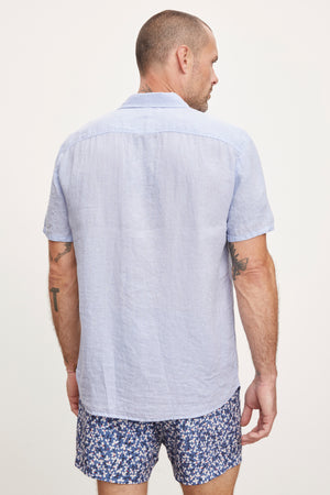 A man seen from behind wears a Velvet by Graham & Spencer MACKIE LINEN BUTTON-UP SHIRT and patterned shorts, standing against a white background.