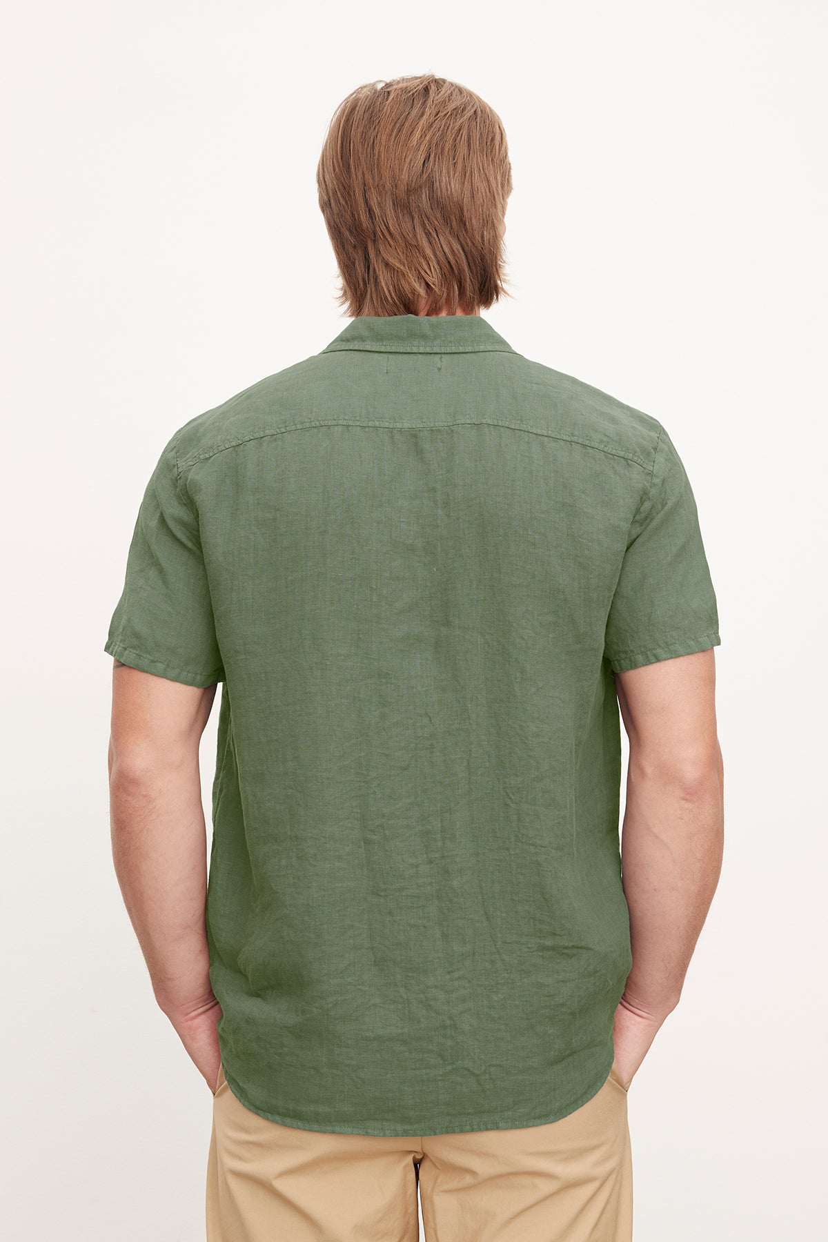   Rear view of a man wearing a Velvet by Graham & Spencer MACKIE LINEN BUTTON-UP SHIRT and beige pants, standing against a plain background. 