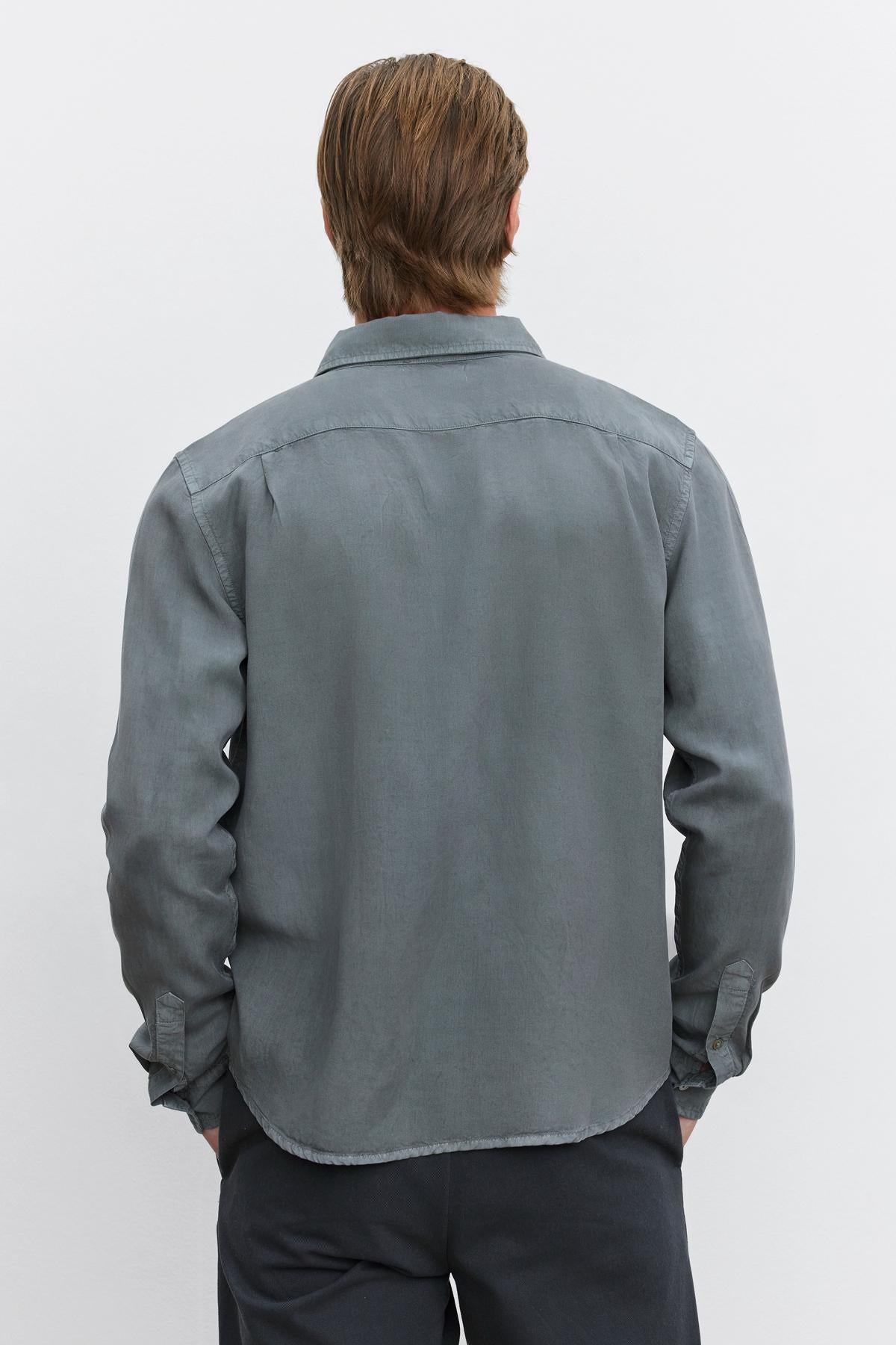   A person with medium-length hair is shown from the back, wearing a long-sleeved, gray WOLF BUTTON-UP SHIRT by Velvet by Graham & Spencer and dark trousers. 