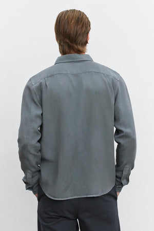 A person with medium-length hair is shown from the back, wearing a long-sleeved, gray WOLF BUTTON-UP SHIRT by Velvet by Graham & Spencer and dark trousers.