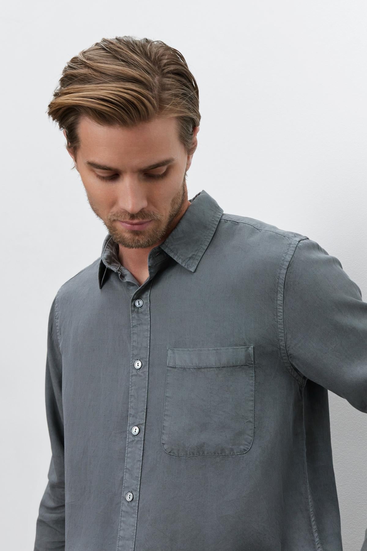 A person with short, light brown hair, wearing a gray Velvet by Graham & Spencer WOLF BUTTON-UP SHIRT with a front pocket, looks down.-37643214913729