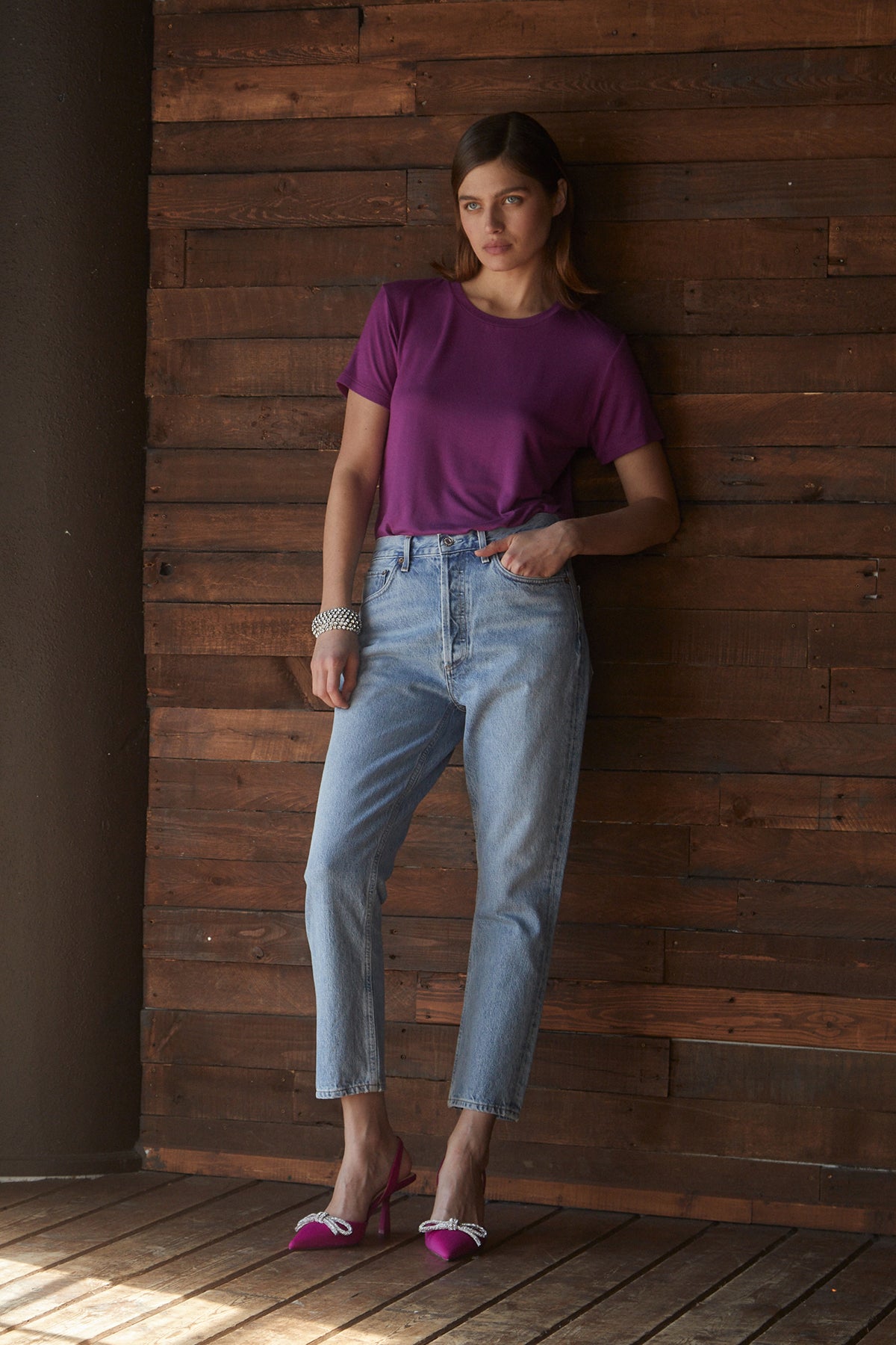   A woman leaning against a wooden wall in a soft Velvet by Jenny Graham SOLANA TEE and jeans. 