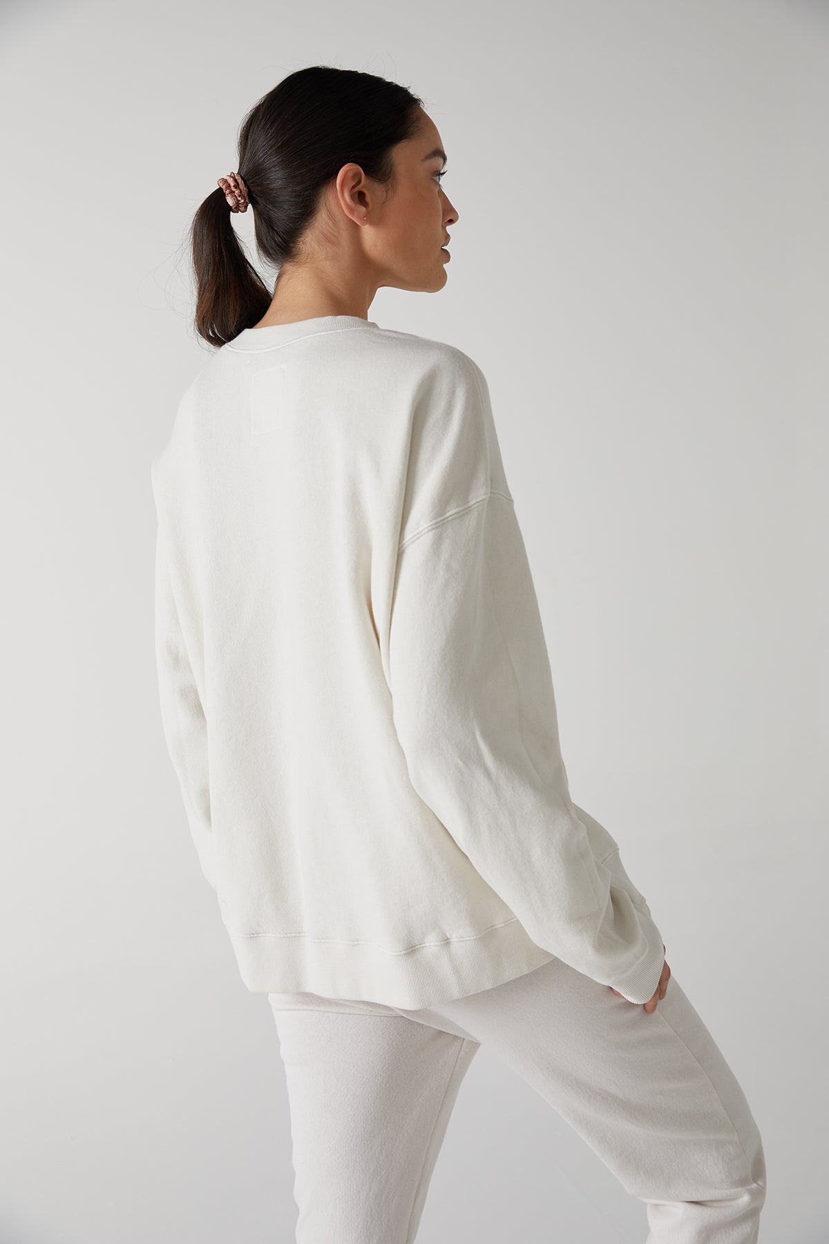   The back view of a woman wearing a Velvet by Jenny Graham ABBOT sweatshirt made of organic cotton and white pants, showcasing the slouch and styling versatility. 