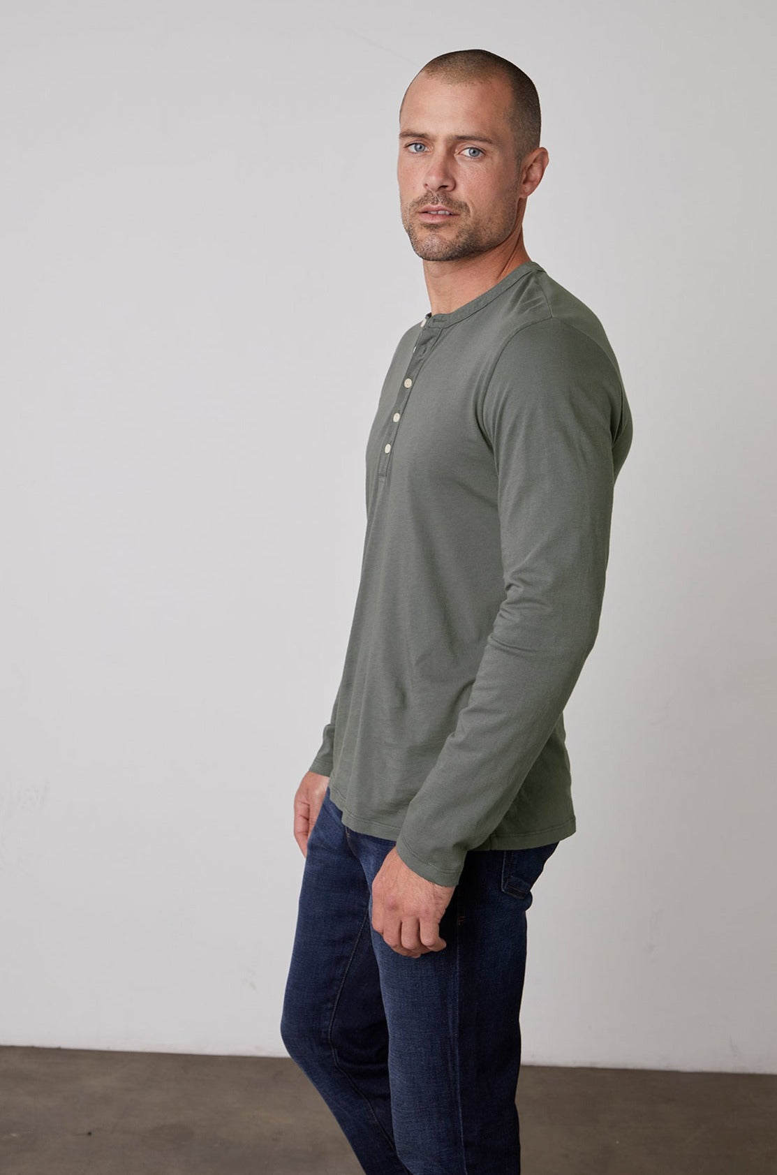A person with short hair wearing a green long-sleeve lightweight ALVARO HENLEY by Velvet by Graham & Spencer and dark jeans stands against a plain white background.-23778972532929
