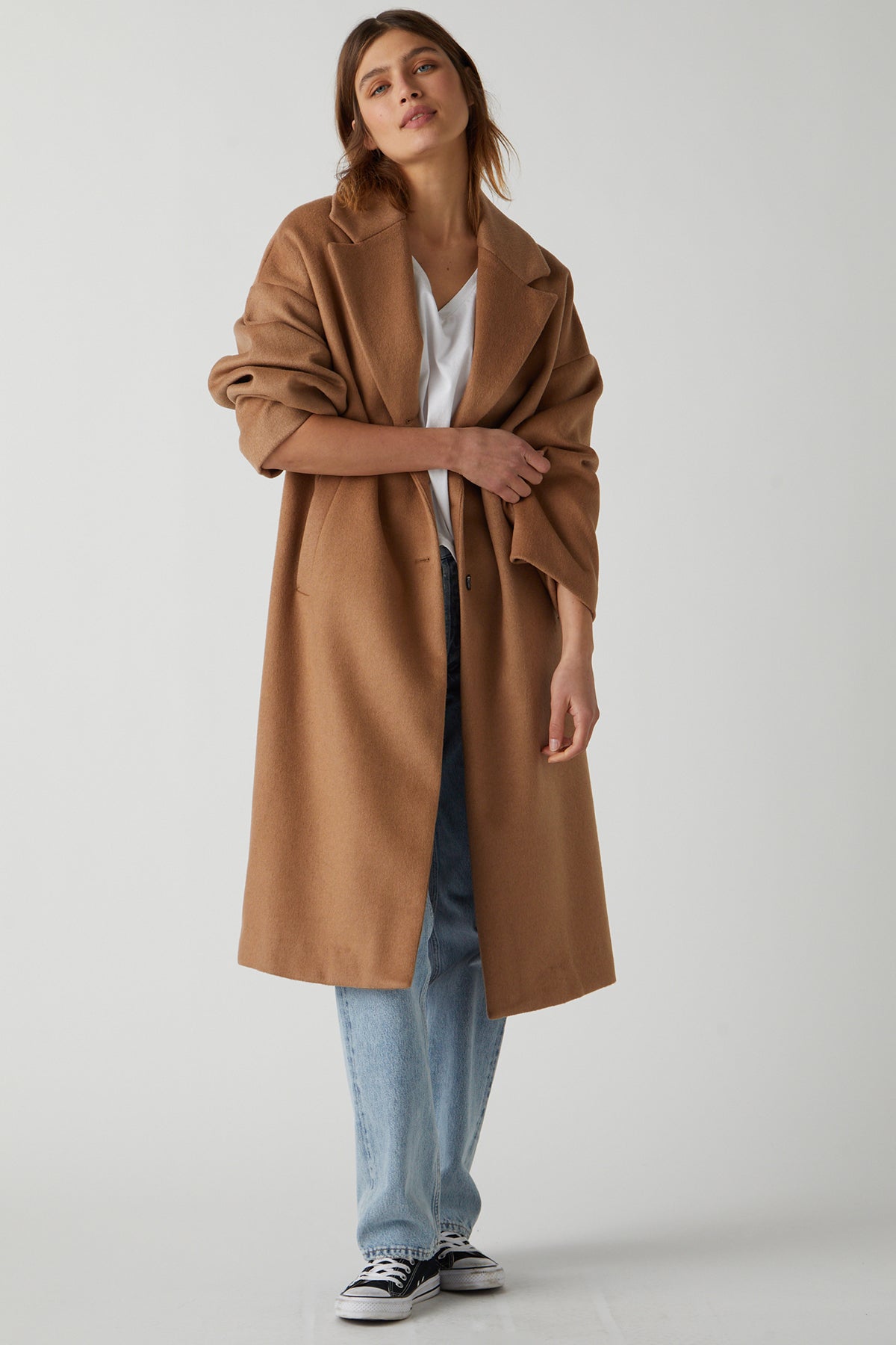   A person wearing a chic HUNTINGTON COAT by Velvet by Jenny Graham, made of soft wool blend, a white t-shirt, light blue jeans, and black and white sneakers stands against a plain backdrop. 