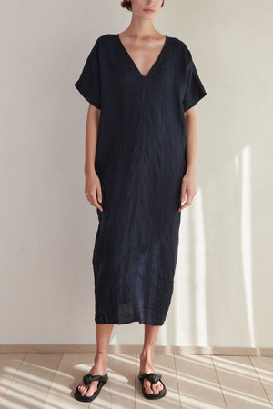 A woman in a Velvet by Jenny Graham Montana Linen Dress stands in a well-lit room, casting a shadow on the tiled floor.