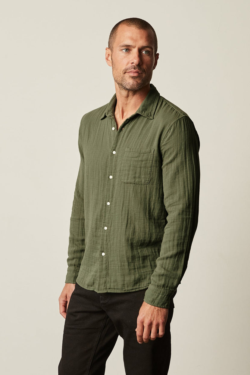 The man is wearing a green Velvet by Graham & Spencer ELTON BUTTON-UP SHIRT and black pants.